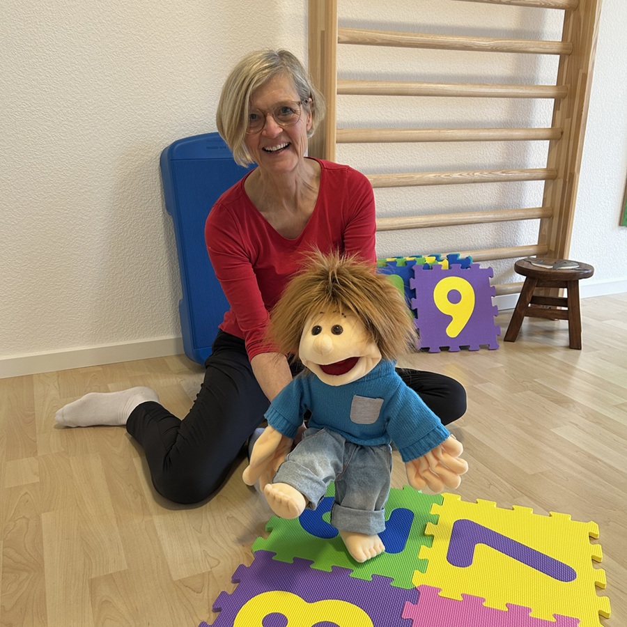 Handpuppe Sam spaziert über eine Puzzlematte mit Zahlen - Friederike Schaeff sitzt dahinter.