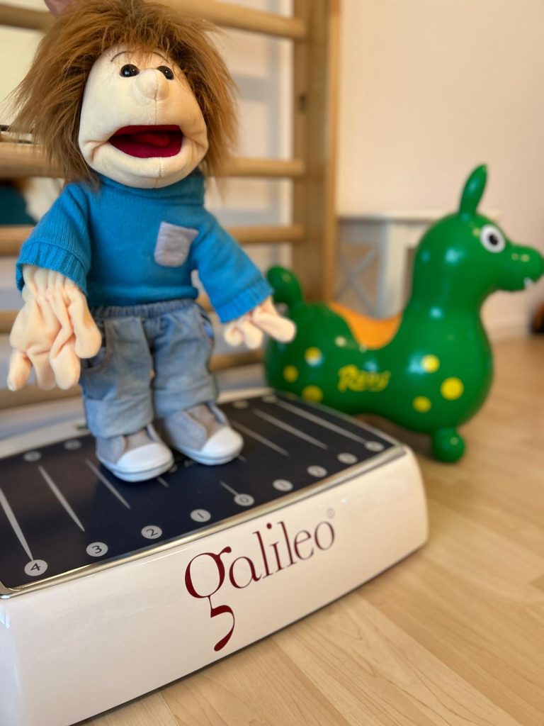 Die Therapiepuppe Sam steht auf der Galileo(R)-Vibrationsplatte.